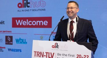 TRN-TLV Tech Week Conference in Albania on March 2023. The GNL CEO, Mr. Roi Shaposhnik smiling on the stage with a background and the speaker stand. All the setup was designed by our studio.